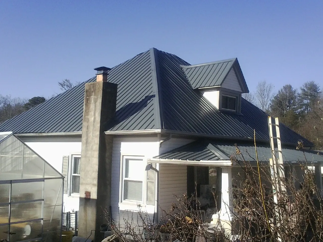 Dark blue standing seam metal roof on a white farmhouse with dormer — Slate & Tile Roof Repair by Roofing Brothers in Marathon