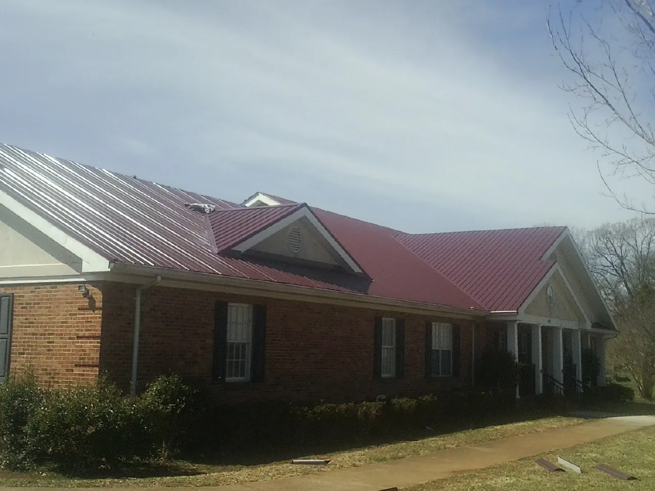Red metal roof with gabled entries on a long brick building, from a Hail Damage Roof Repair job in Marathon