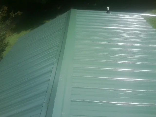 New green metal panels meeting at the ridge of a roof — Flat Roof Repair work by our crew in Marathon