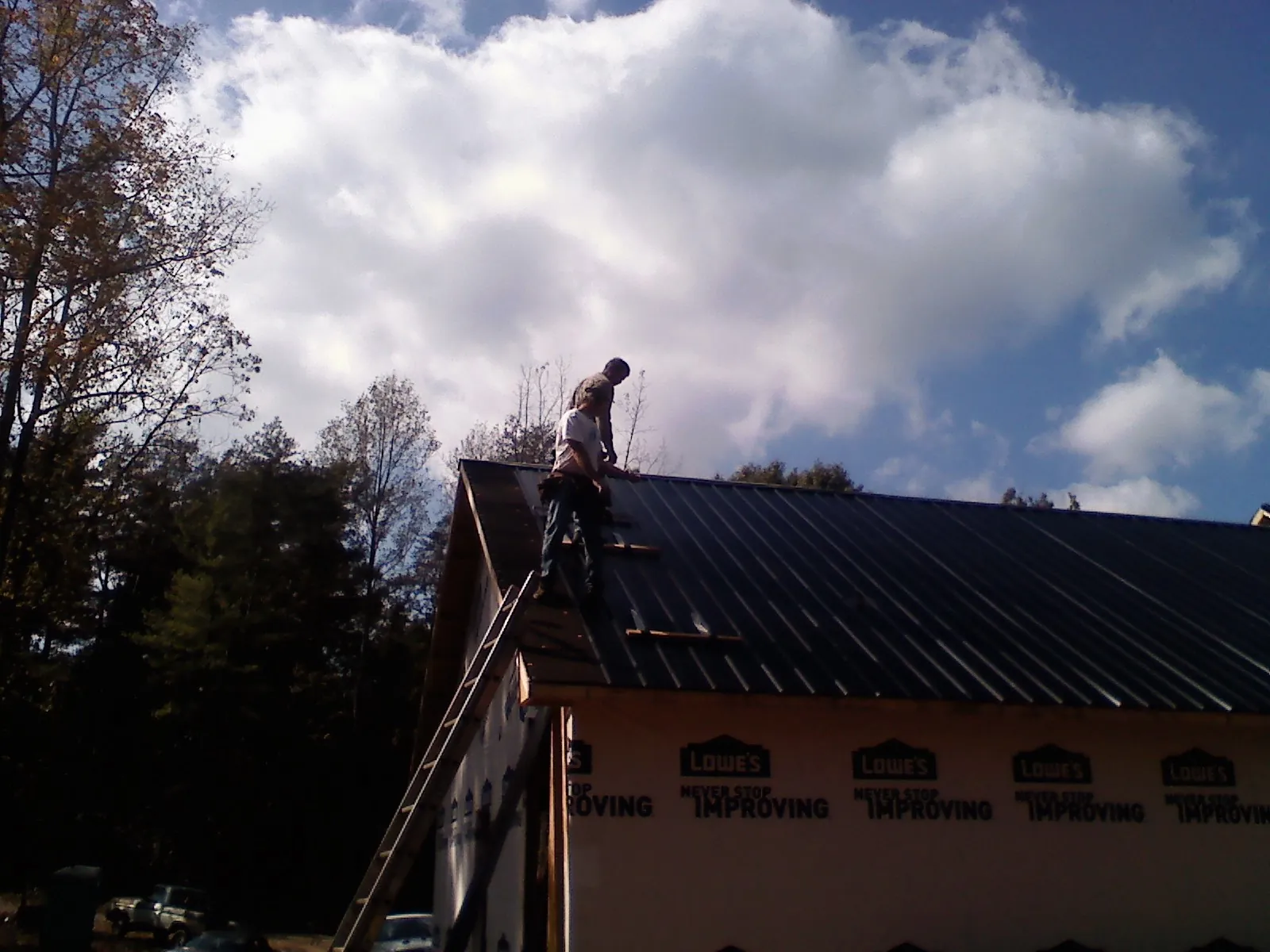 Roofer fastening dark metal panels high against a cloudy sky, from a Roof Inspection job in Marathon