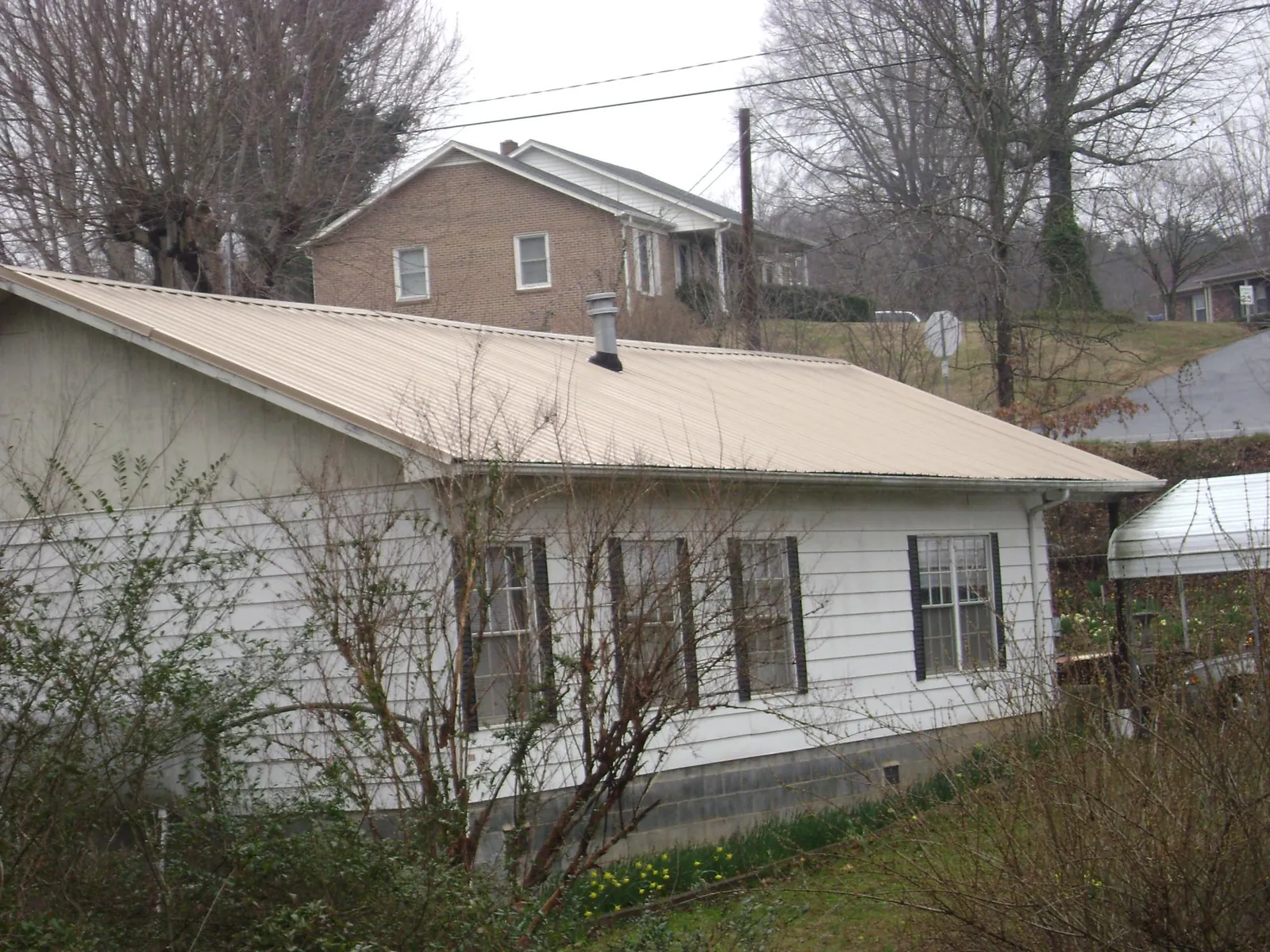 Tan metal roof on a white sided house set into a hillside — Commercial Roofing by Roofing Brothers in Marathon